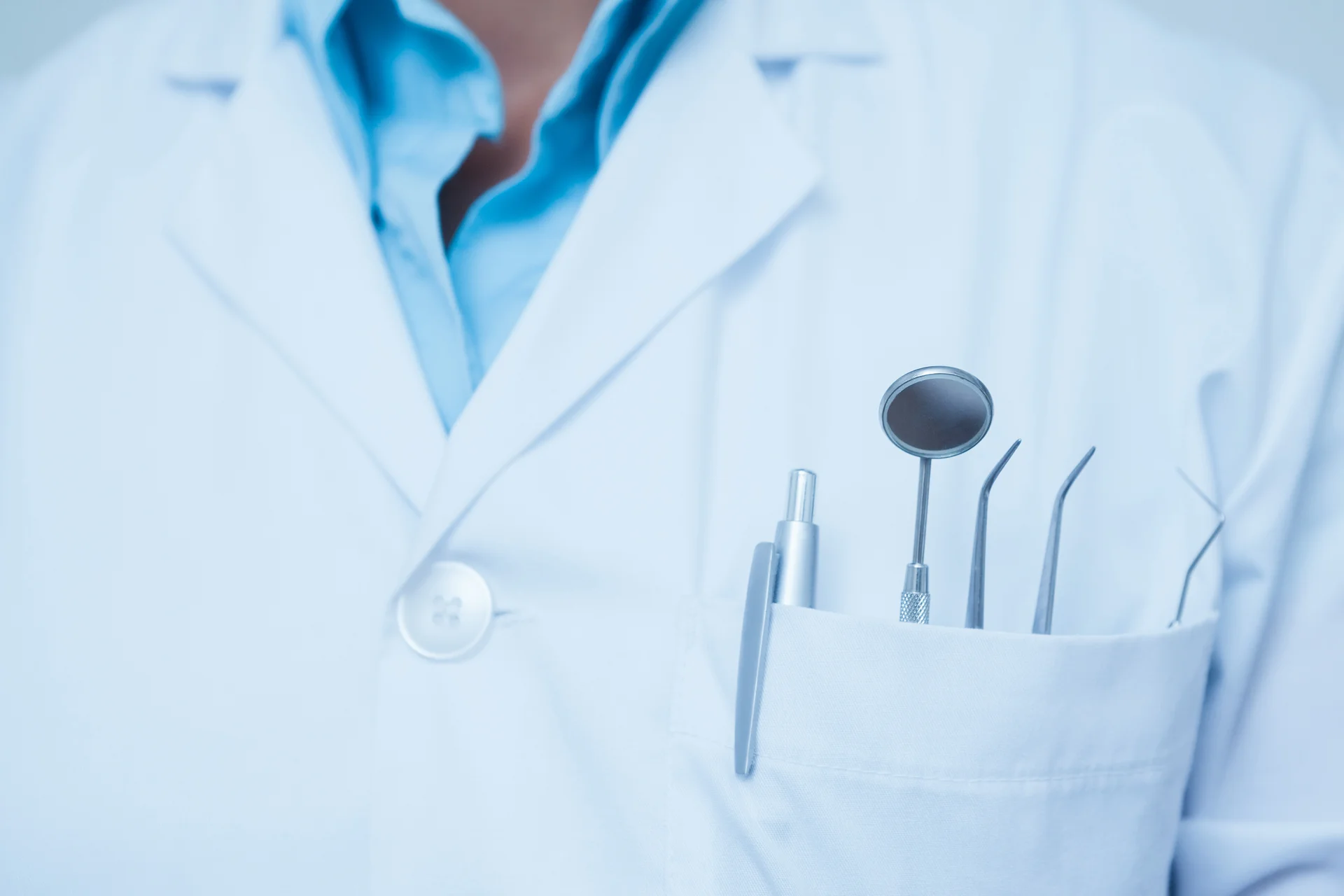 Dental Instruments in a Dentist's Pocket Close-up of dental instruments in a white coat pocket, including a mirror and dental probes.